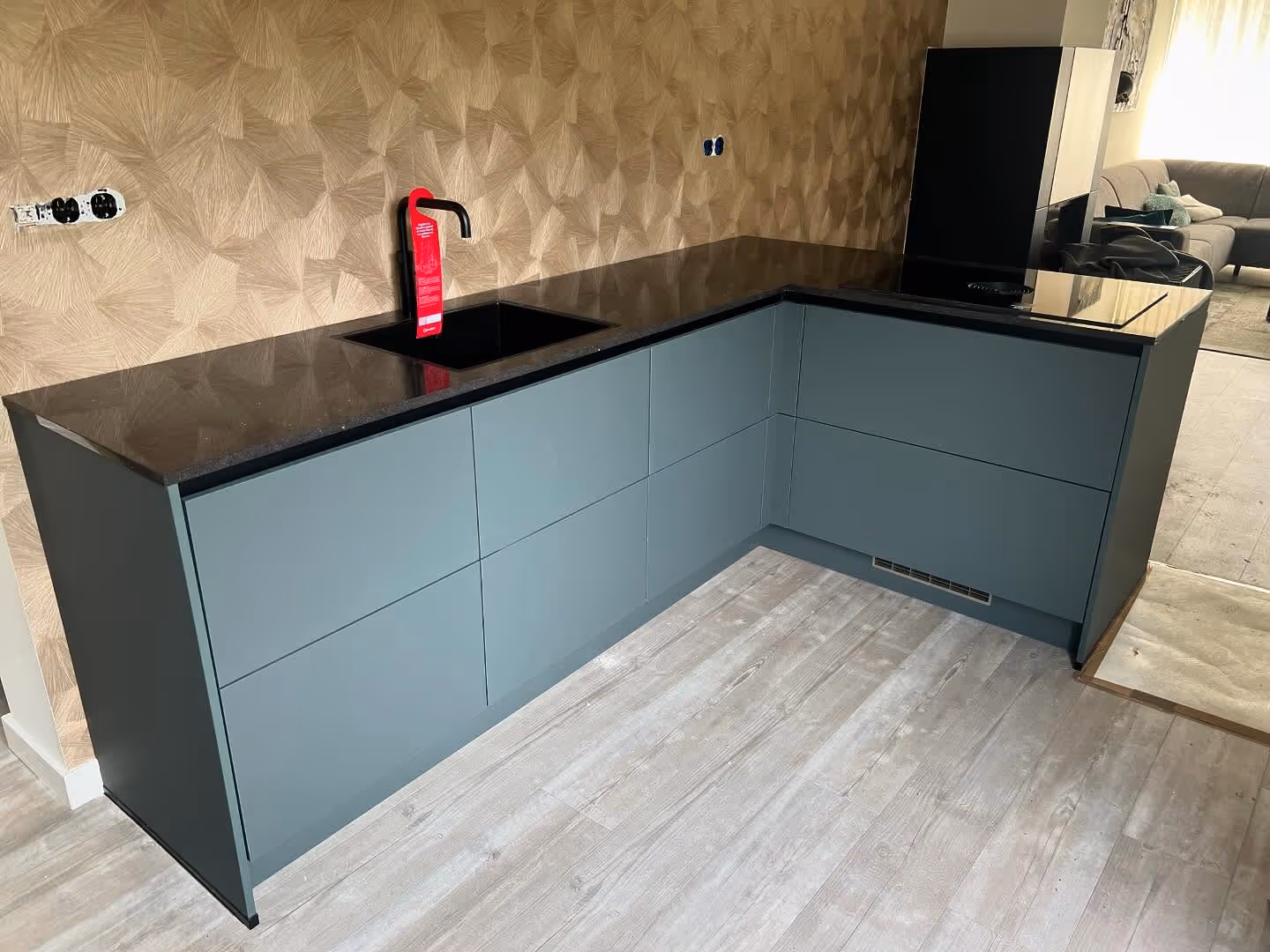 A cozy interior shot shows a black leather sofa next to a light wood open-shelf bench with a plant and books, below a light wood slatted staircase and a framed bird artwork.
